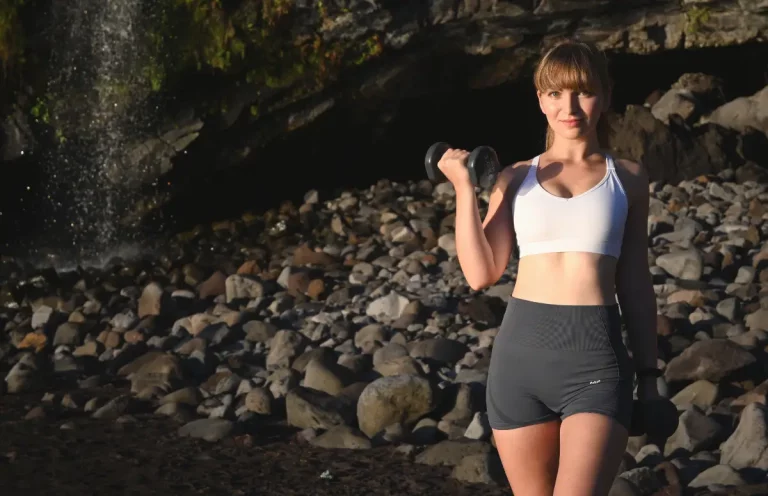 Lift and Bloom founder holding two dumbbells at the beach in front of a waterfall